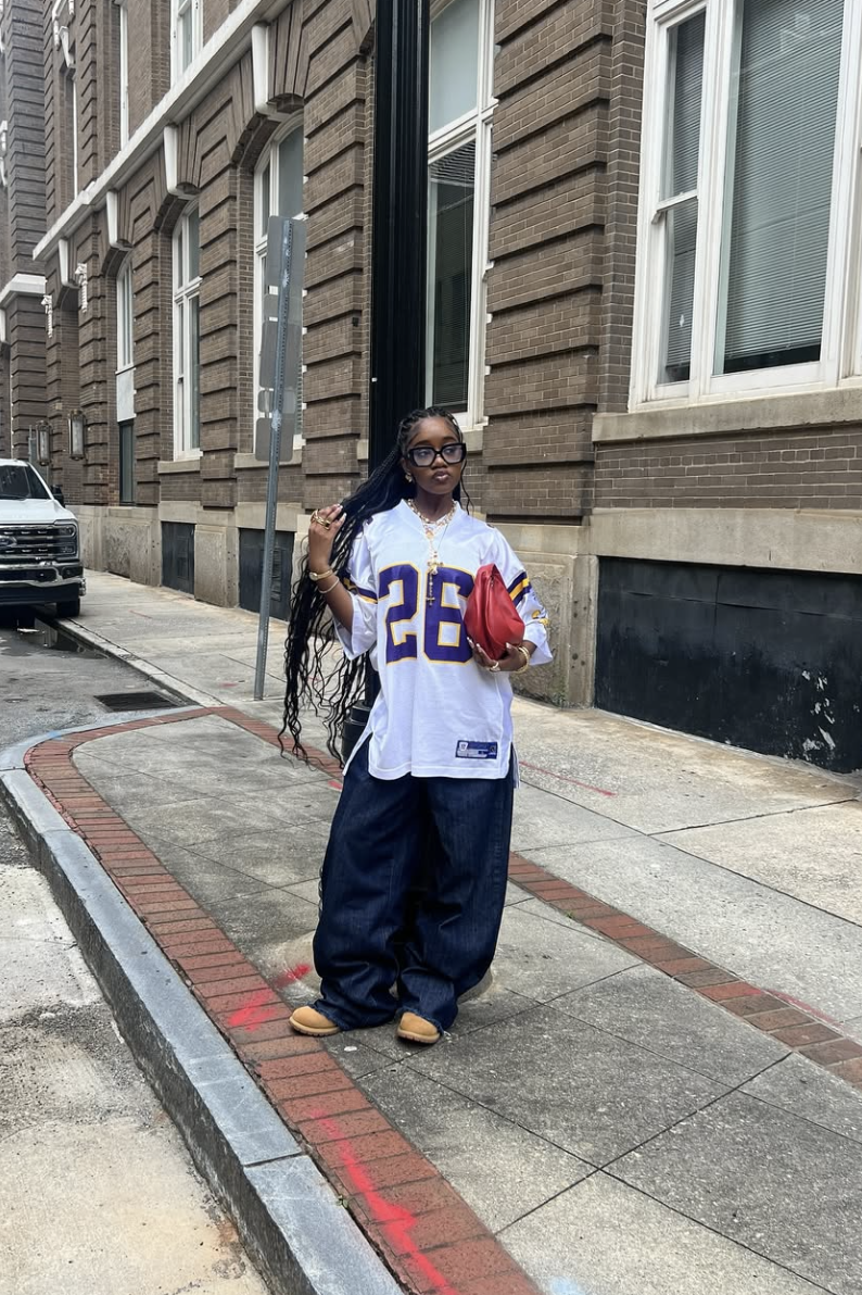 A woman wearing oversized dark-wash baggy jeans and a white graphic t-shirt with tan boots to demonstrate a relaxed streetwear outfit formula.