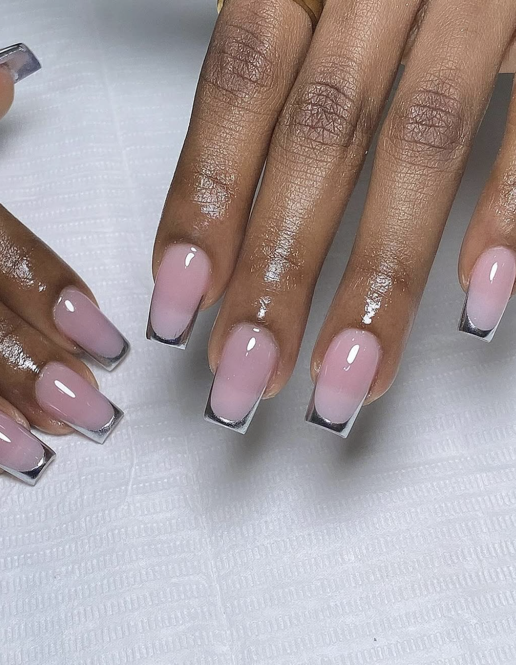 Close-up of short squoval nails featuring a metallic silver chrome micro French tip over a glossy sheer pink base.