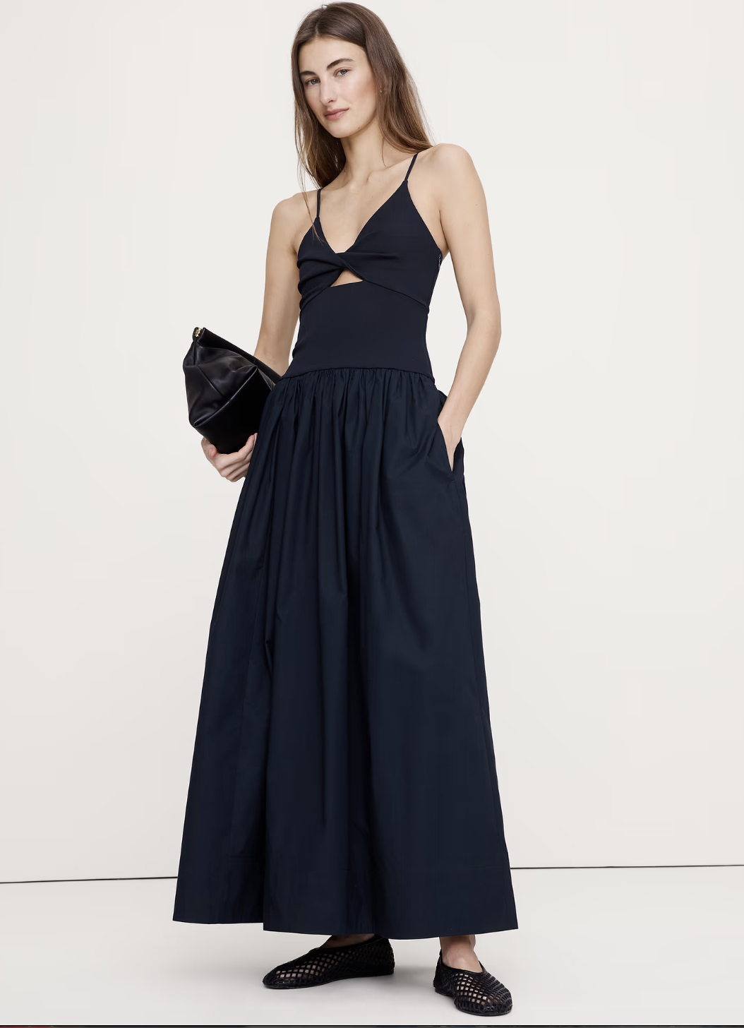 A woman wearing a sleeveless navy blue maxi dress with a sweetheart neckline, front cutout detail, and a voluminous pleated skirt.
