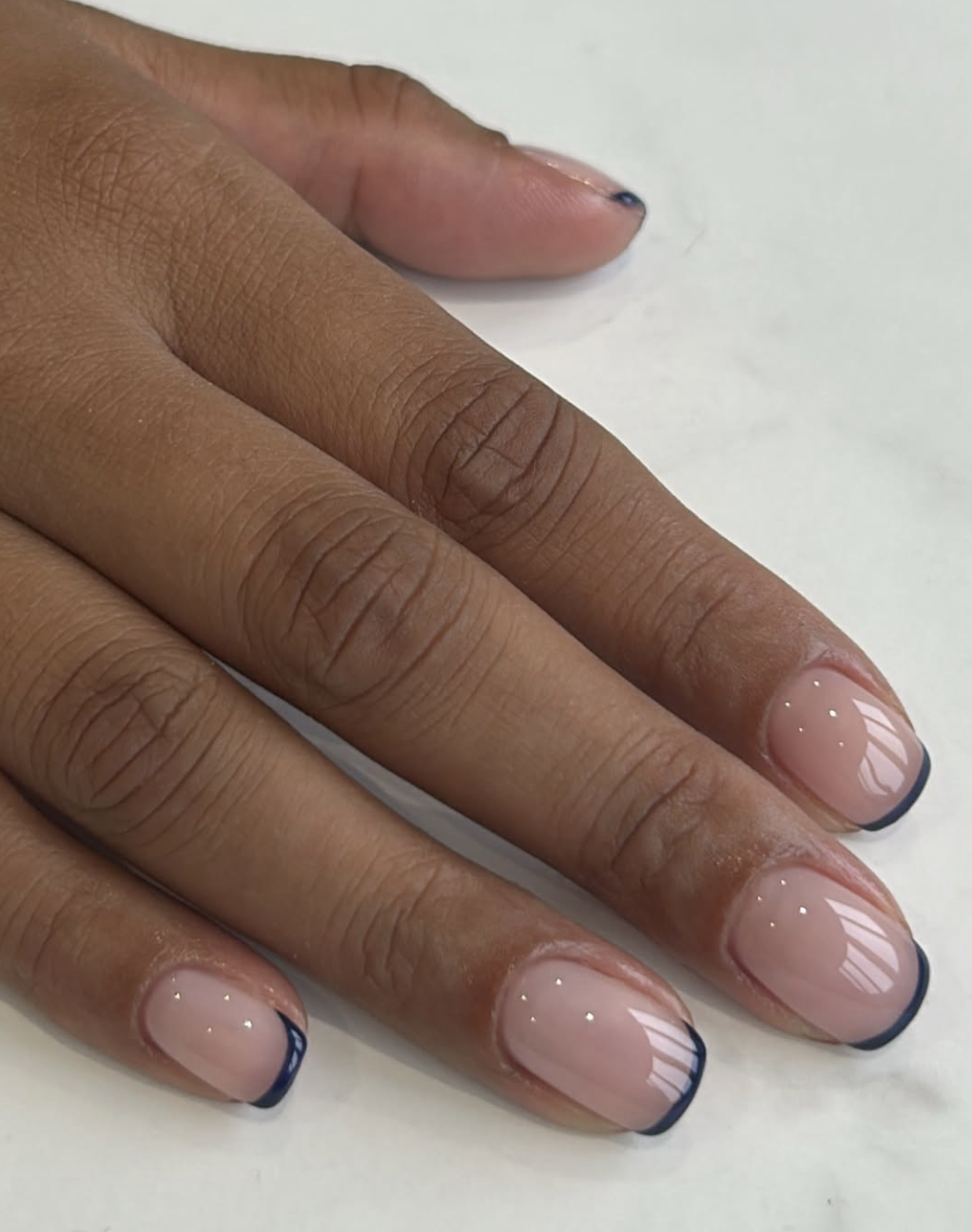 Close-up of short rounded nails featuring an inky navy blue micro French tip over a glossy sheer nude base.