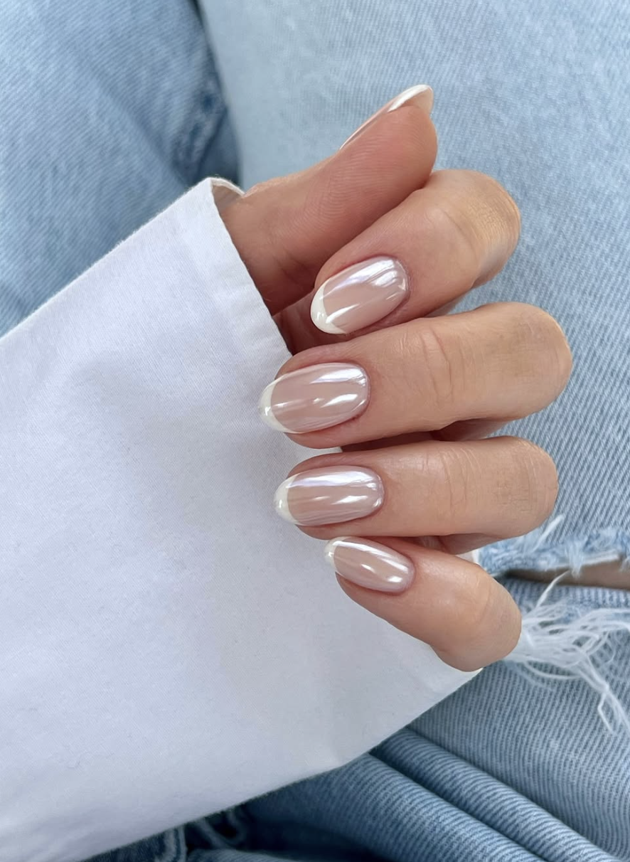 Long, oval-shaped nails featuring a sheer, natural base with crisp white French tips, all finished with a luminous pearl chrome glaze overlay.