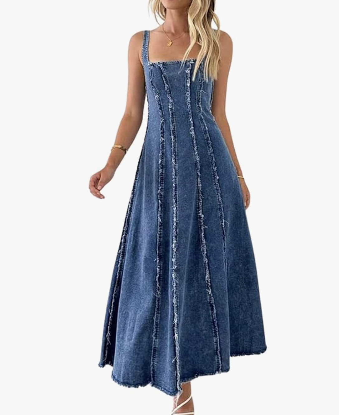 A woman wearing a dark-wash denim maxi dress with vertical distressed seam detailing and a raw hem, styled as a modern A-line silhouette for a spring wardrobe for women in their 50s.