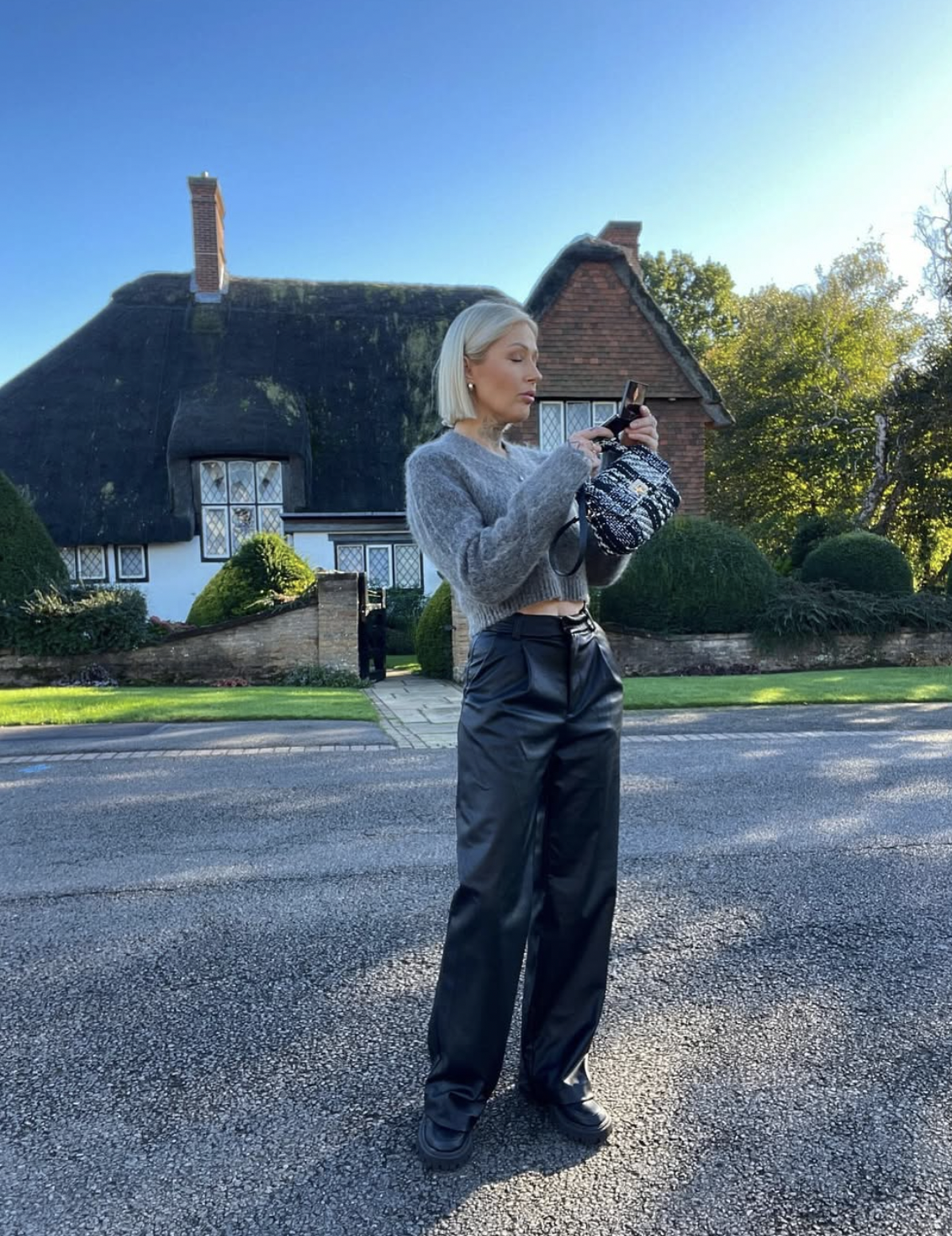 Woman wearing black straight-leg leather pants, a cropped gray fuzzy sweater and chunky black boots outdoors