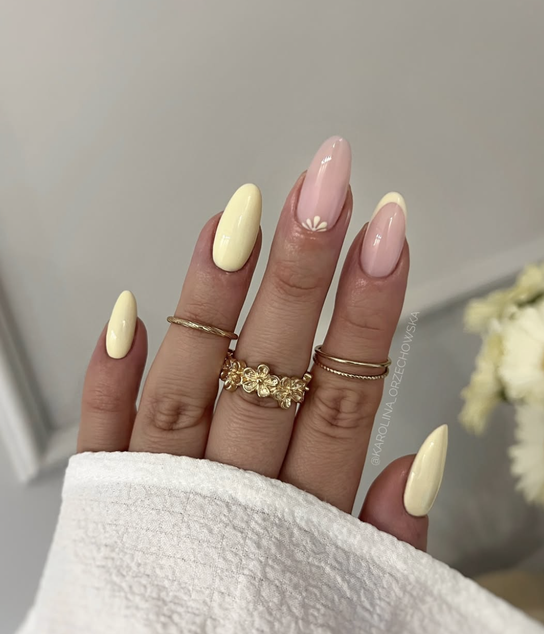 A high-feminine spring manicure by @karolina_orzechowska featuring glossy butter-yellow almond nails and a sheer accent nail with a dainty white hand-painted flower.