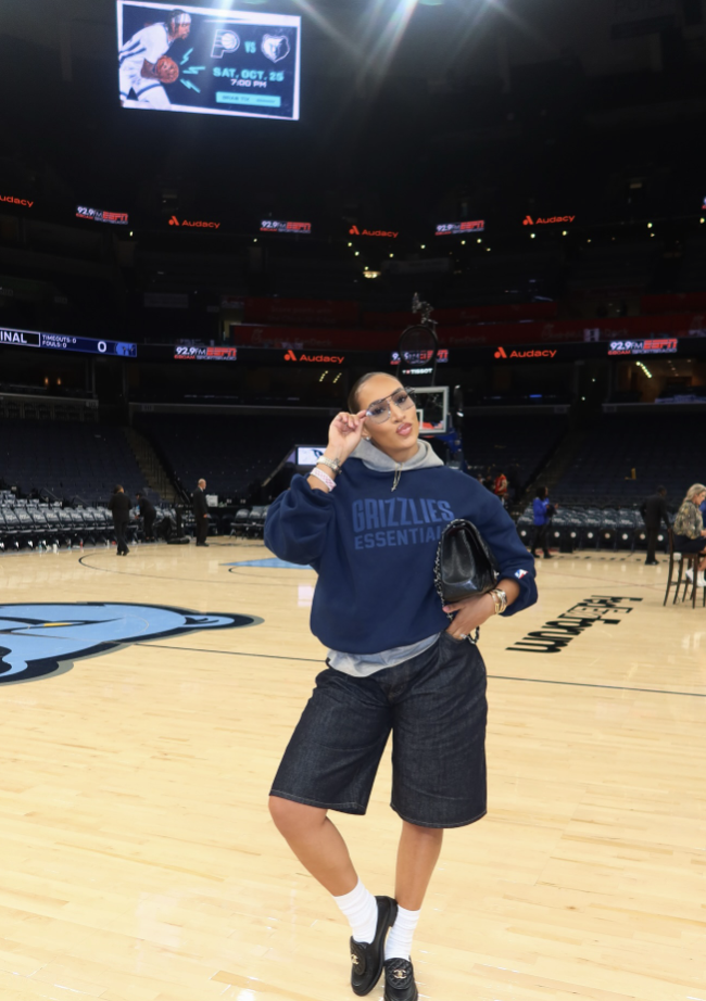 Woman courtside wearing an oversized team sweatshirt with long black shorts, crew socks and sneakers.