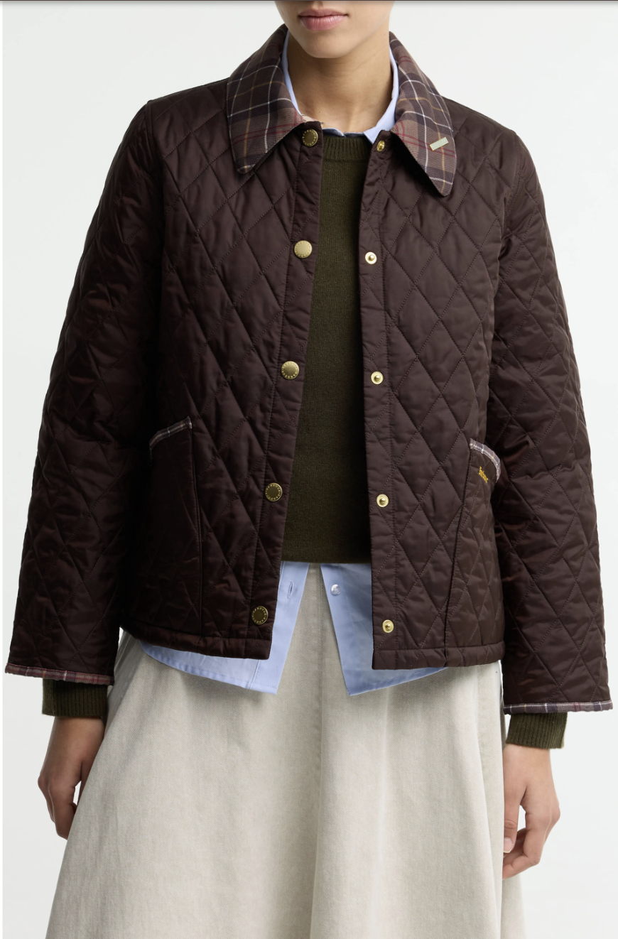 Woman over 60 styling an olive quilted jacket with a striped knit, dark-wash jeans and loafers for fall.