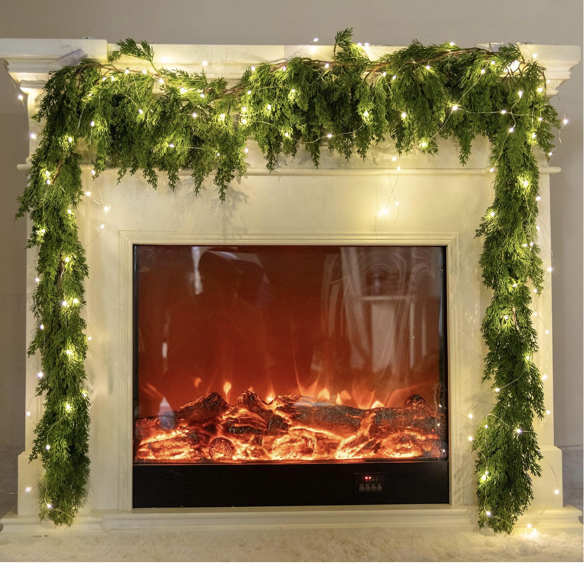 Cream fireplace mantel with a cedar garland and fairy lights draped across the top and down both sides.
