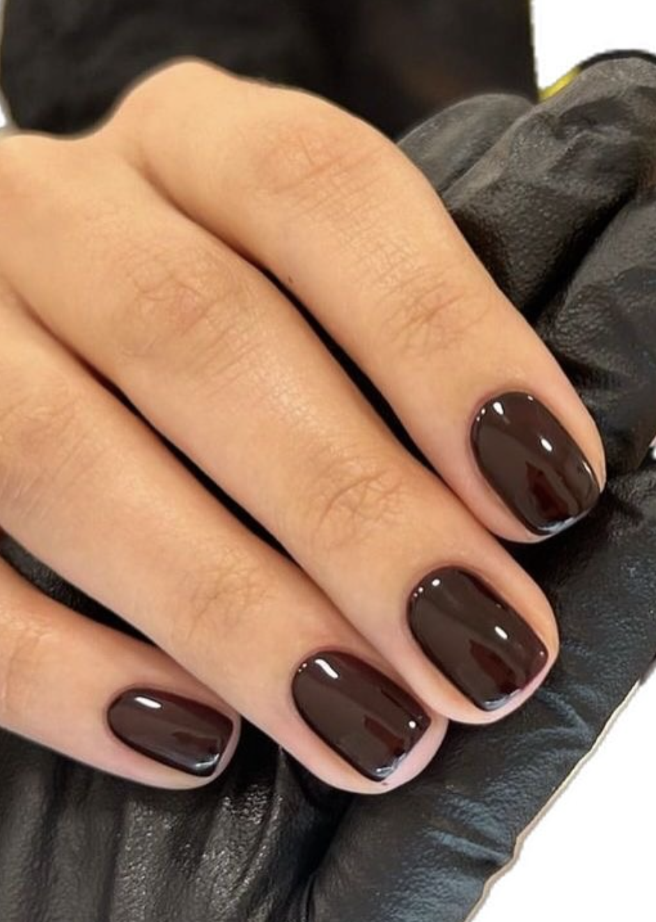 A close-up of short squoval nails featuring a glossy milk chocolate brown polish over a black leather background.