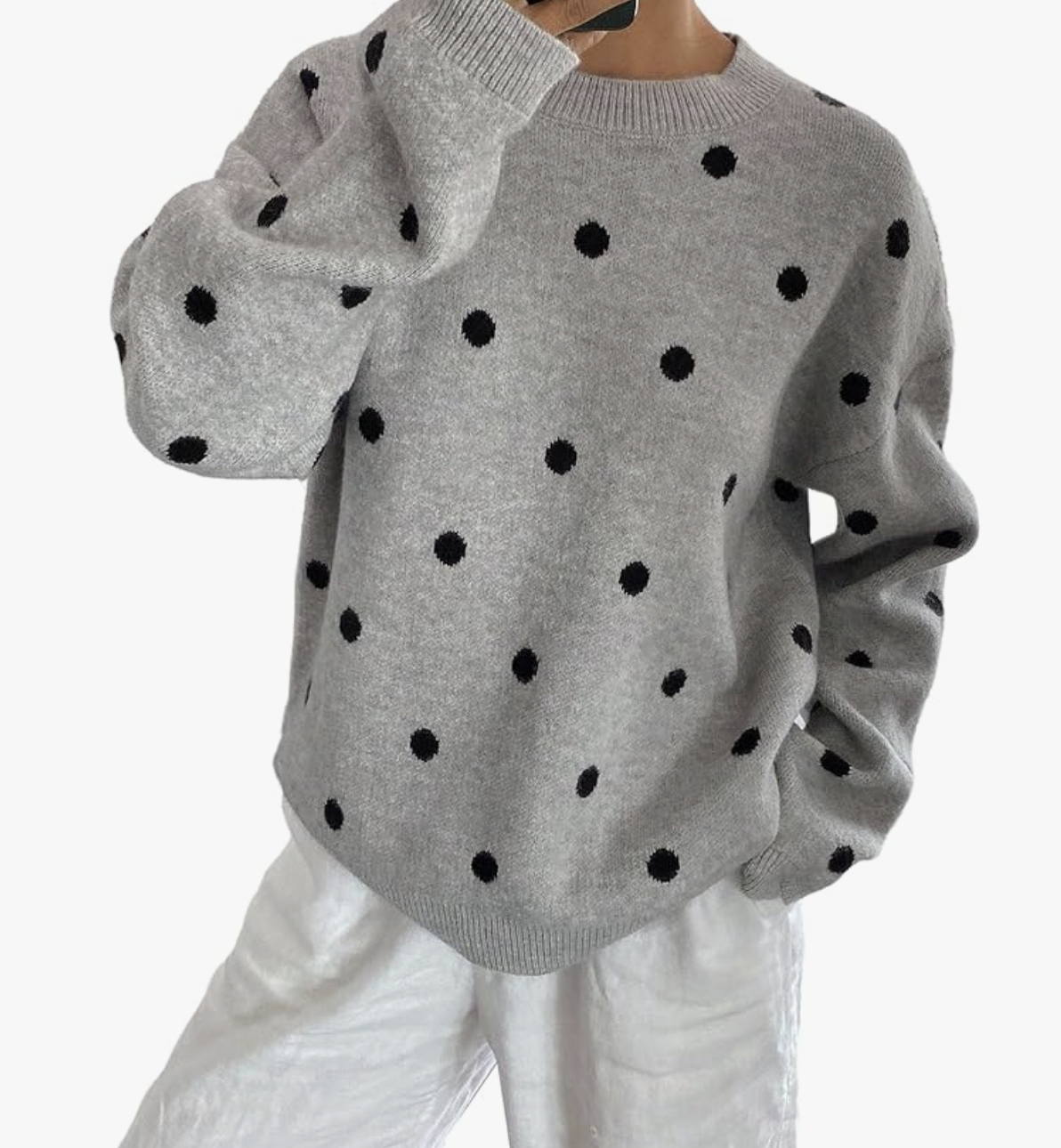 A close-up of a woman wearing a cozy, oversized grey crewneck sweater with large black polka dots.