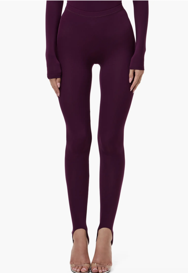 Front view of a model wearing high-waisted eggplant purple stirrup leggings from Naked Wardrobe with matching long-sleeve top.