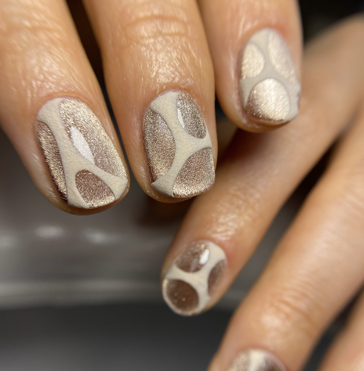 Close-up of a hand showcasing a modern velvet manicure on long almond nails, featuring a shimmering champagne gold magnetic cat-eye base with smooth, matte-finished negative space cutout overlays.