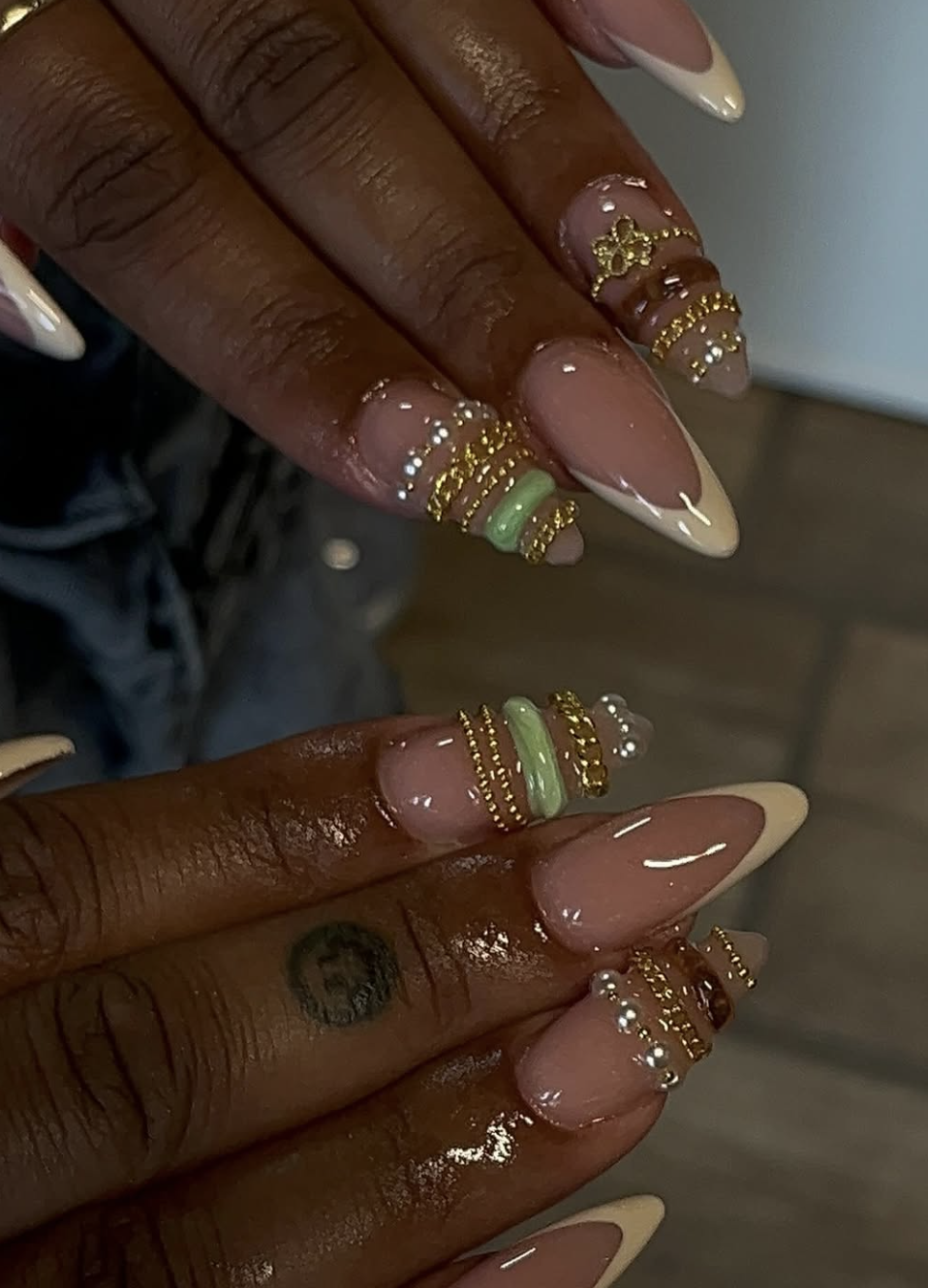 Almond-shaped nails with nude base, sage green 3D gel accents, and gold butterfly jewelry charms.