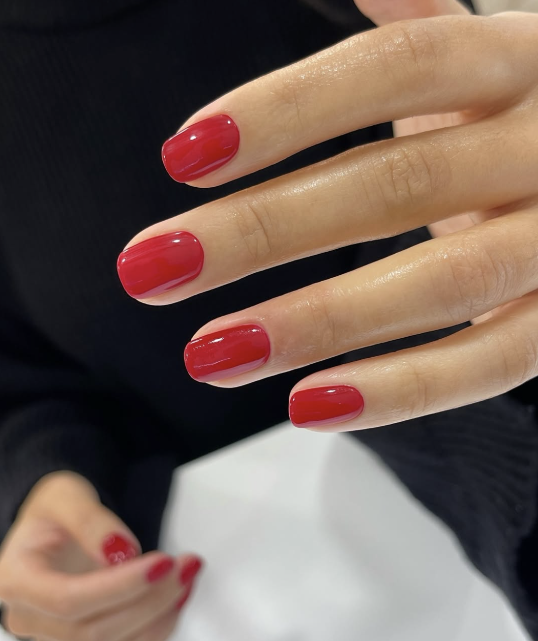 A classic bright red Italian manicure on short squoval nails, painted with a narrow unpainted gap along each side to elongate the nail plate.