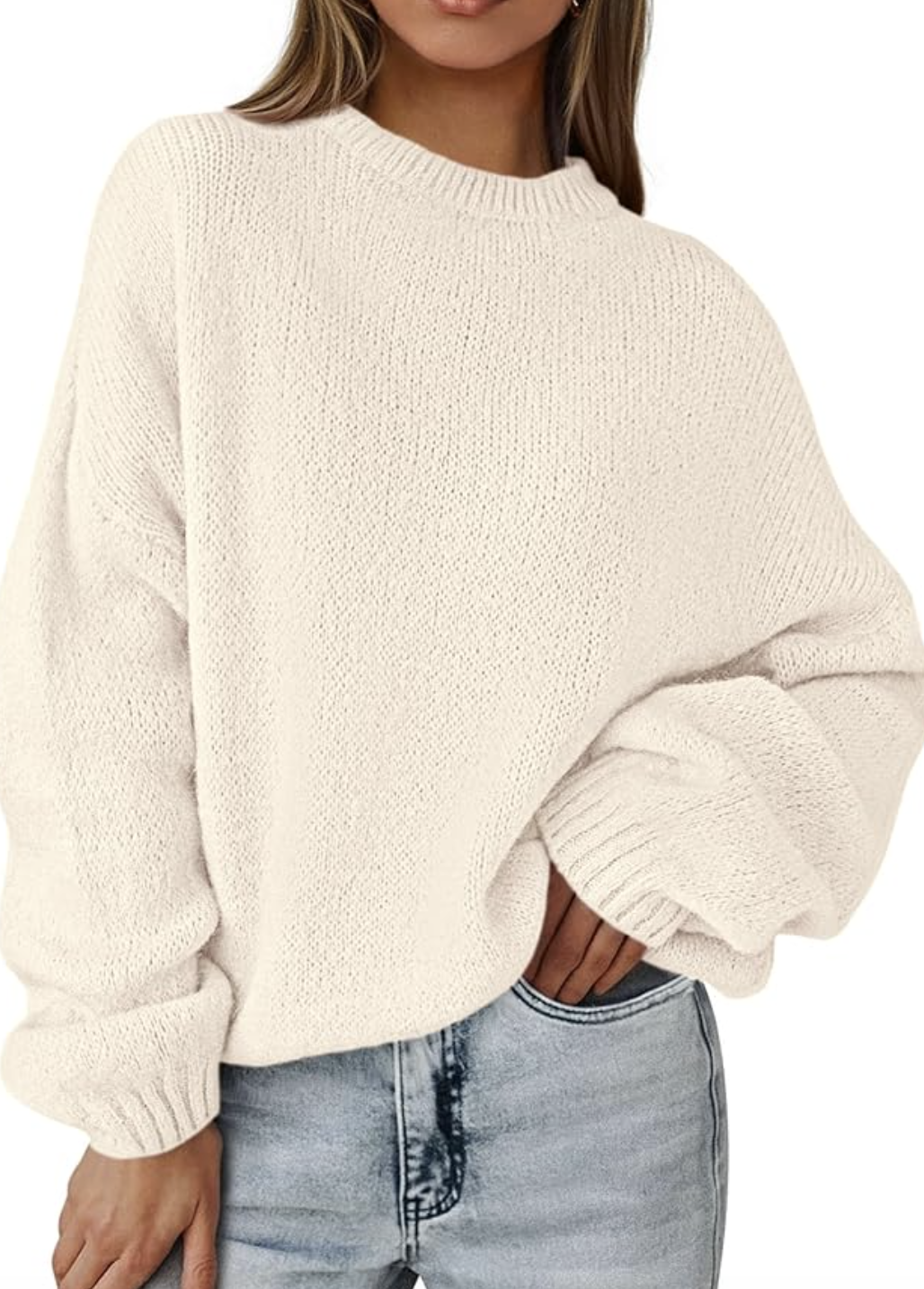 A product photo of a woman wearing the Amazon Oversized Sweater in cream white, featuring a chunky crewneck knit and relaxed fit, tucked into light-wash jeans.