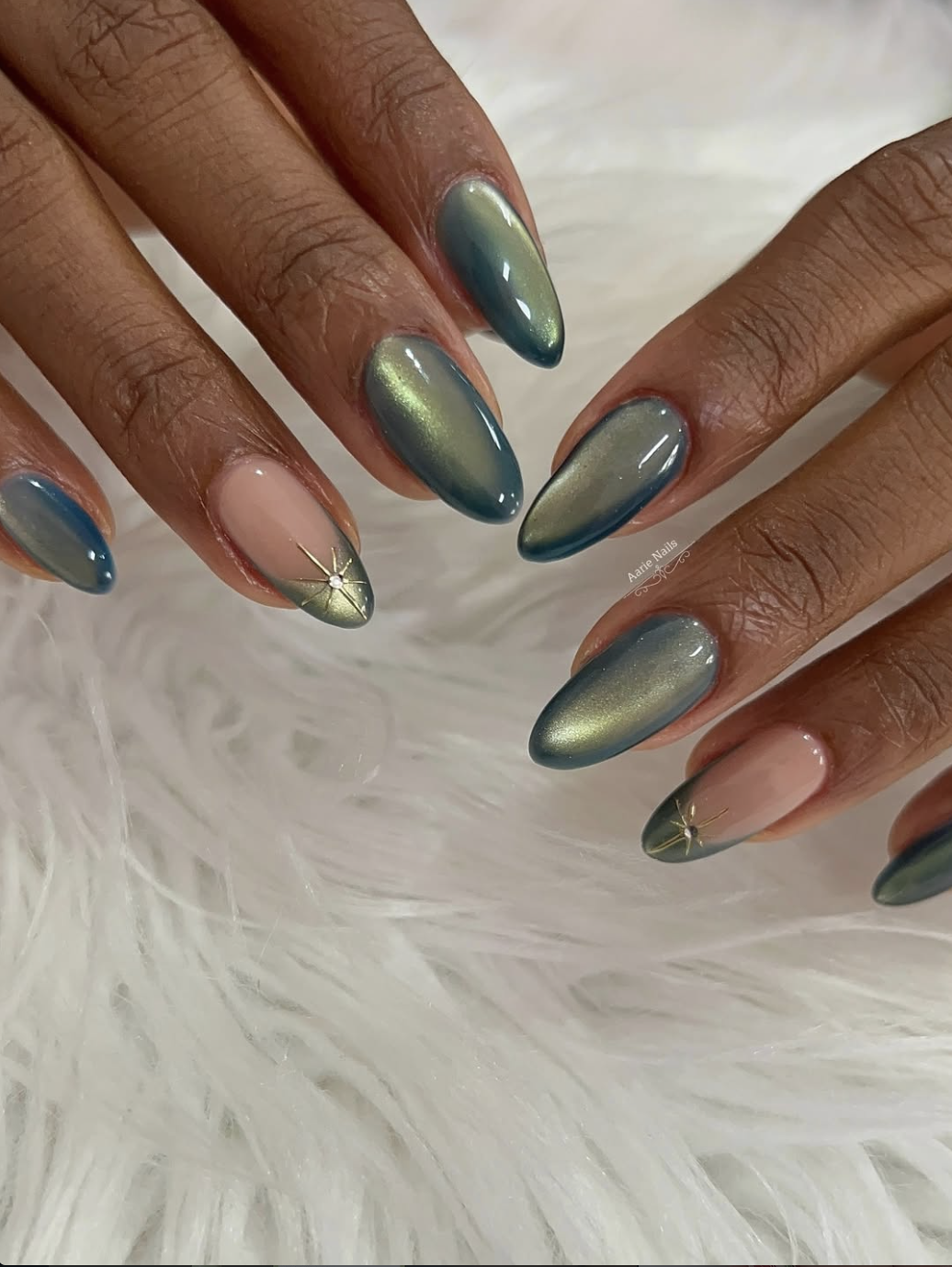 Long almond-shaped nails with a green velvet cat-eye finish, featuring a small, elegant gold star detail on the ring finger.