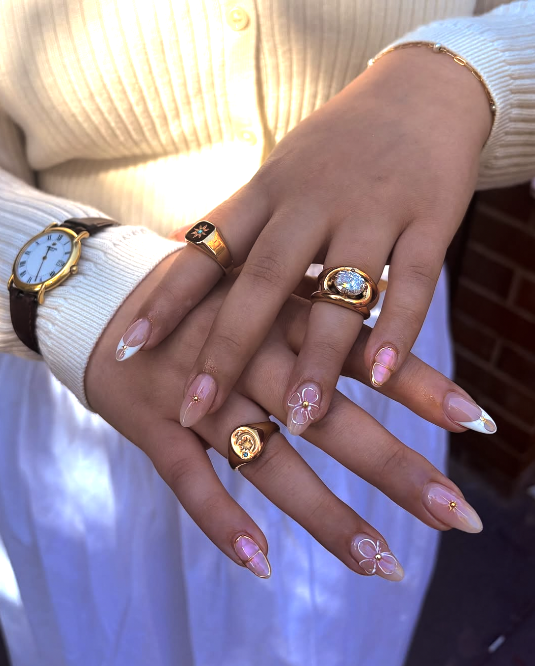 Sheer milky-white nails with delicate hand-painted white flowers and tiny gold celestial sunburst accents, paired with chunky gold rings.