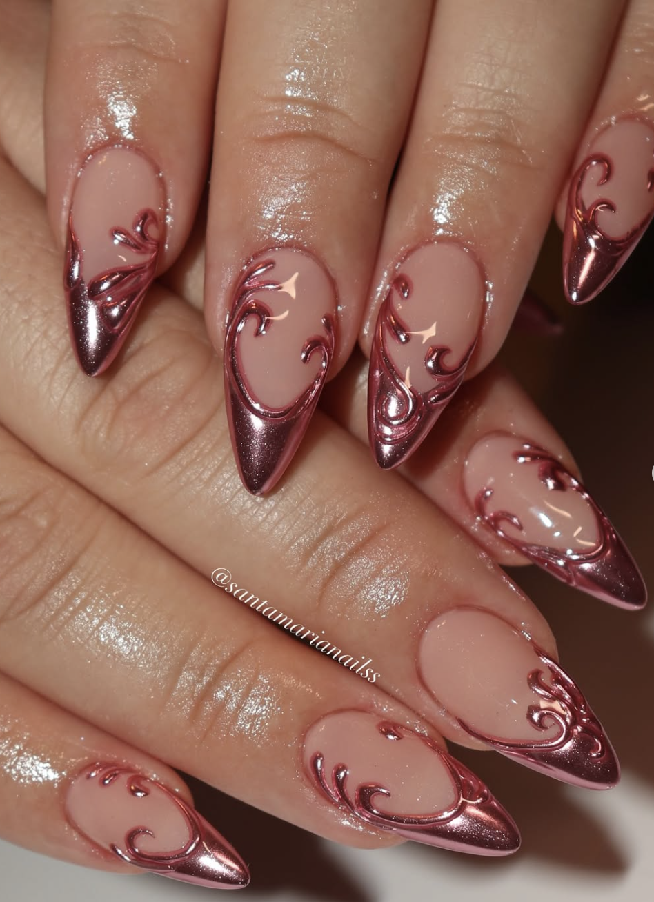 A close-up of almond-shaped nails with a sheer base and raised, 3D rose gold chrome filigree swirl designs.