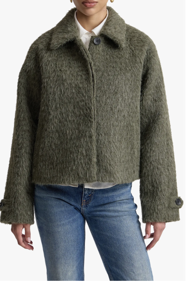A close-up of a structured, cropped olive green woolly jacket styled with light-wash jeans.
