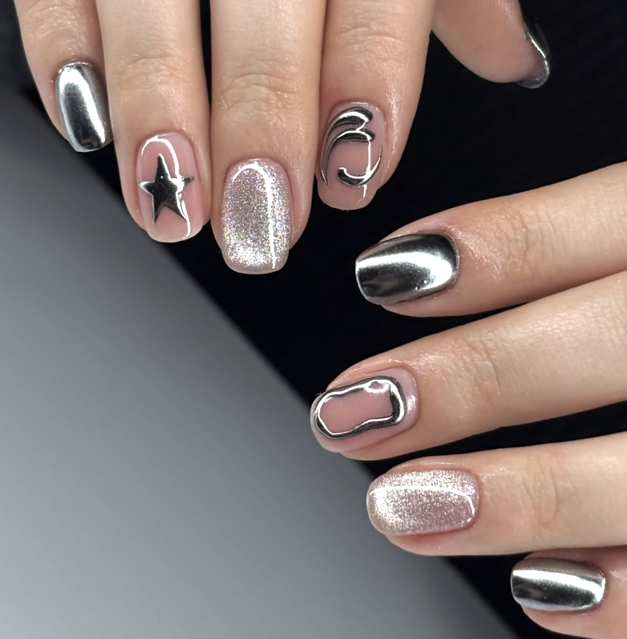 A close-up of short nails featuring a mix of high-shine silver chrome, holographic glitter, and a 3D metallic star accent on a neutral base.