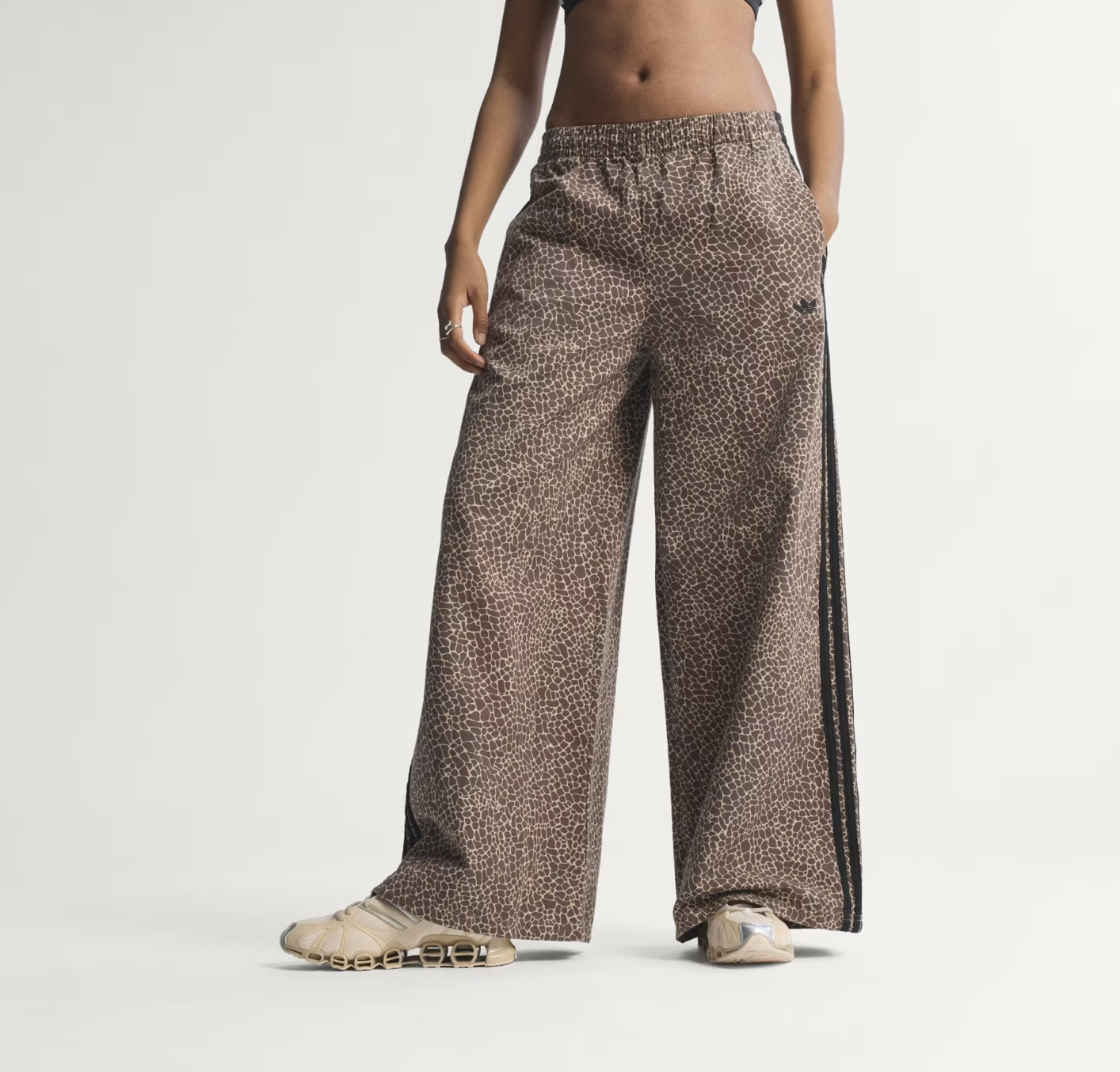 A detailed view of the black adidas Originals Adilenium track pants, featuring an ultra-wide-leg silhouette and signature white side stripes, perfect for a high-low minimalist spring outfit.