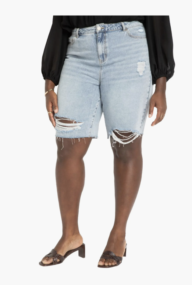 A woman wearing black ELOQUII City Shorts with a wide A-line leg and a high-waisted tailored fit, designed to flatter thick thighs and an apron belly.