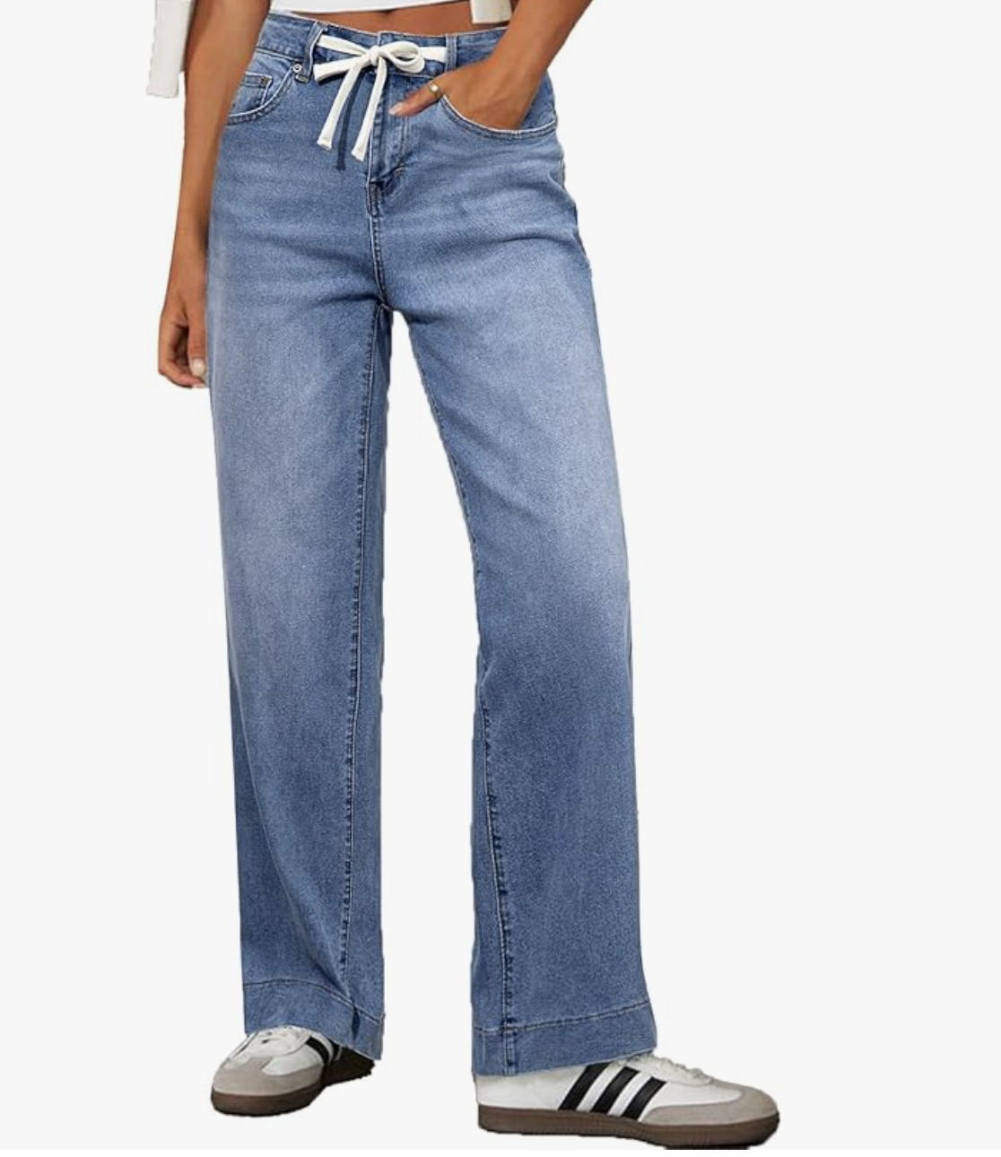 A close-up of a person wearing medium-wash wide-leg jeans with a drawstring waist, paired with white and black Adidas Samba sneakers.