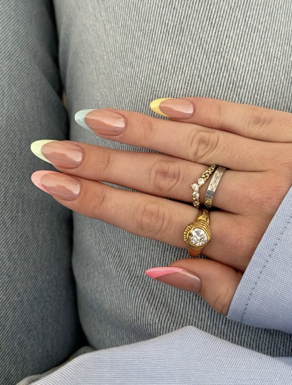 High-feminine almond nails by @thelittleproject_ featuring a glossy nude base with thin, multi-colored pastel French tips in mint green, butter yellow, and soft peach.