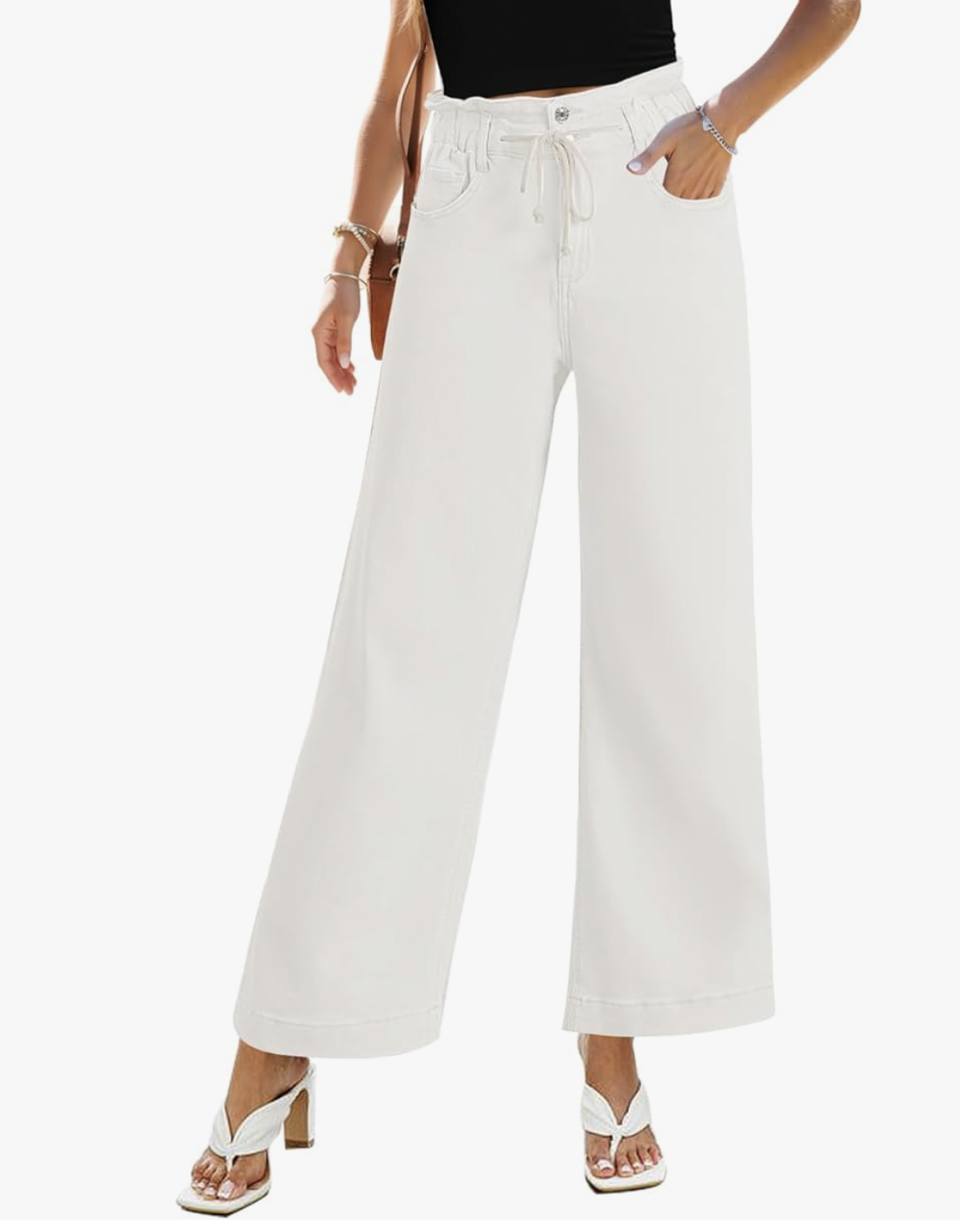 A close-up of a person wearing white high-waisted, wide-leg ankle jeans with a drawstring waist, paired with white heeled slide sandals.