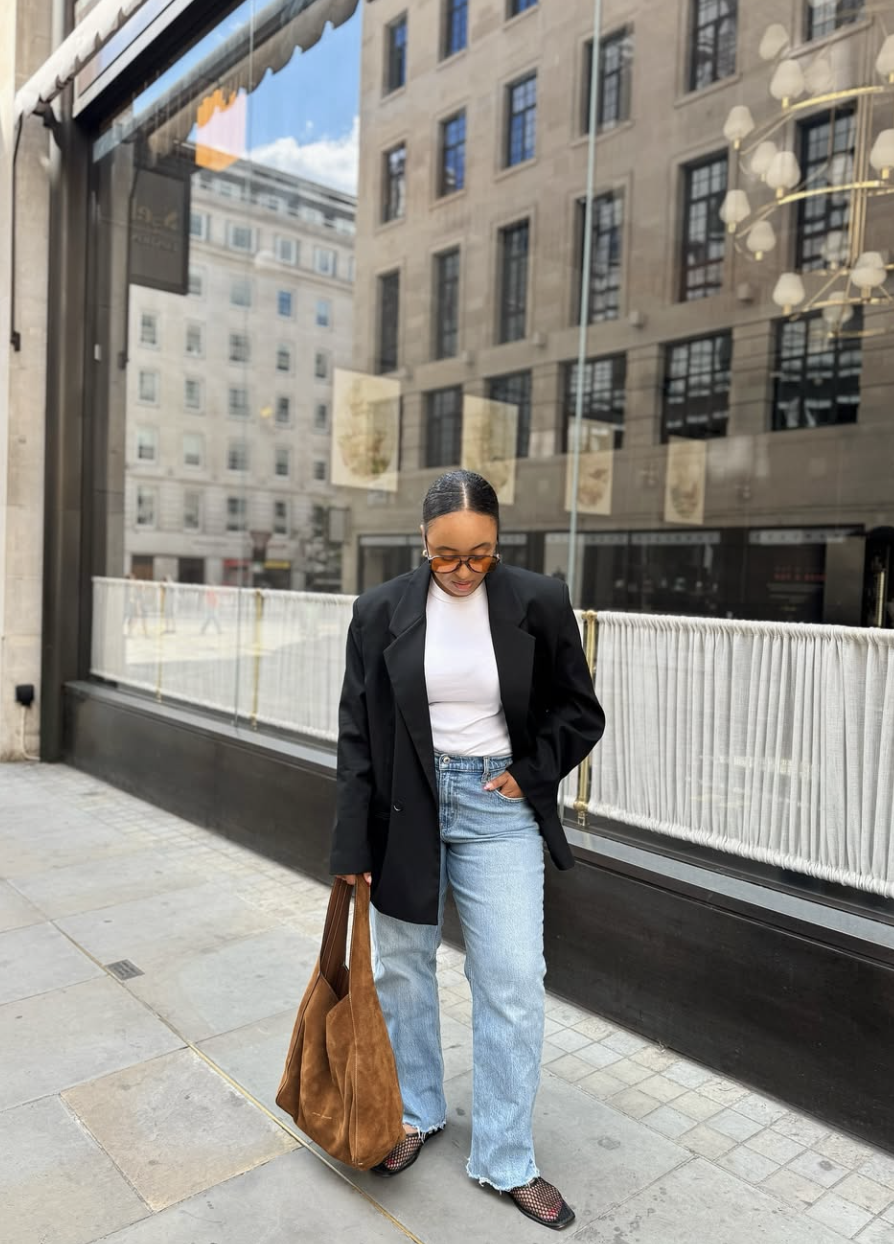 A fashion editor-inspired outfit featuring a crisp white t-shirt tucked into relaxed straight-leg blue jeans, layered with a long black coat and accessorized with a large tan leather tote bag.