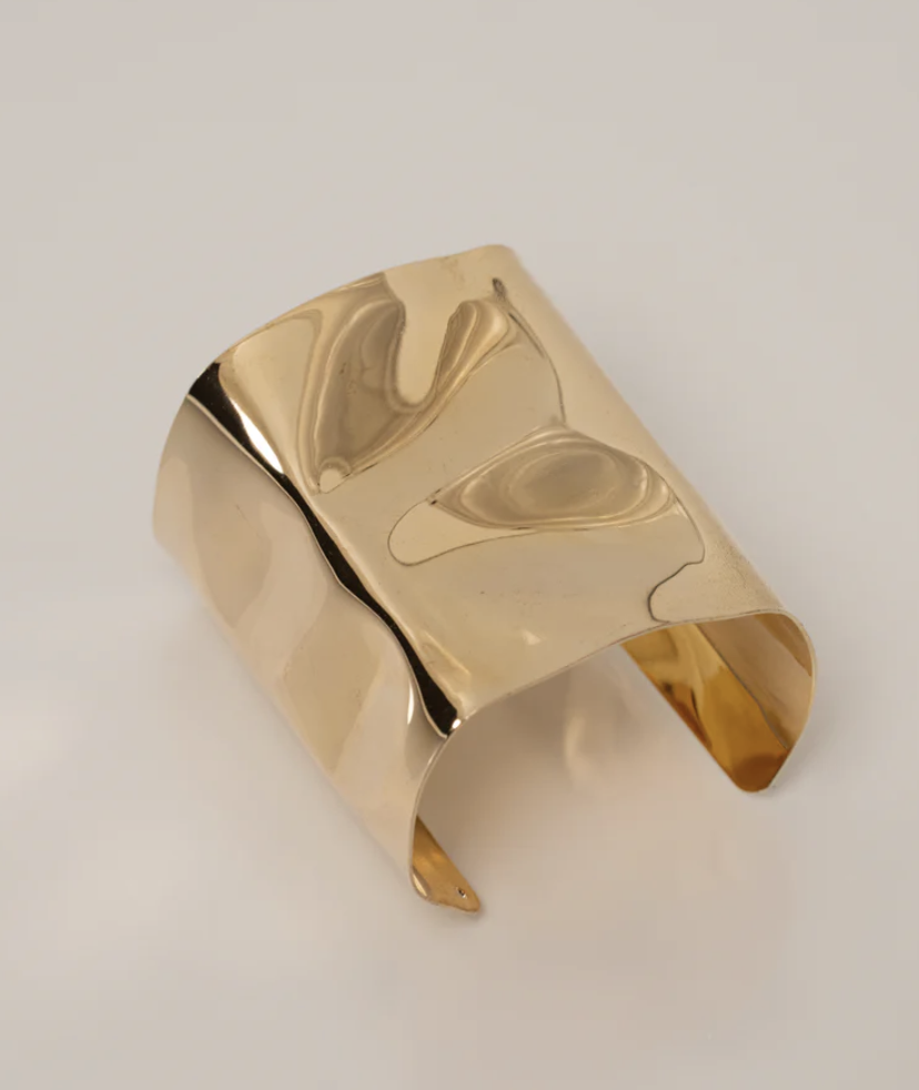 A high-polish gold sculptural cuff bracelet from JLUXLABEL, styled as a statement accessory for a Mediterranean resort vacation look.