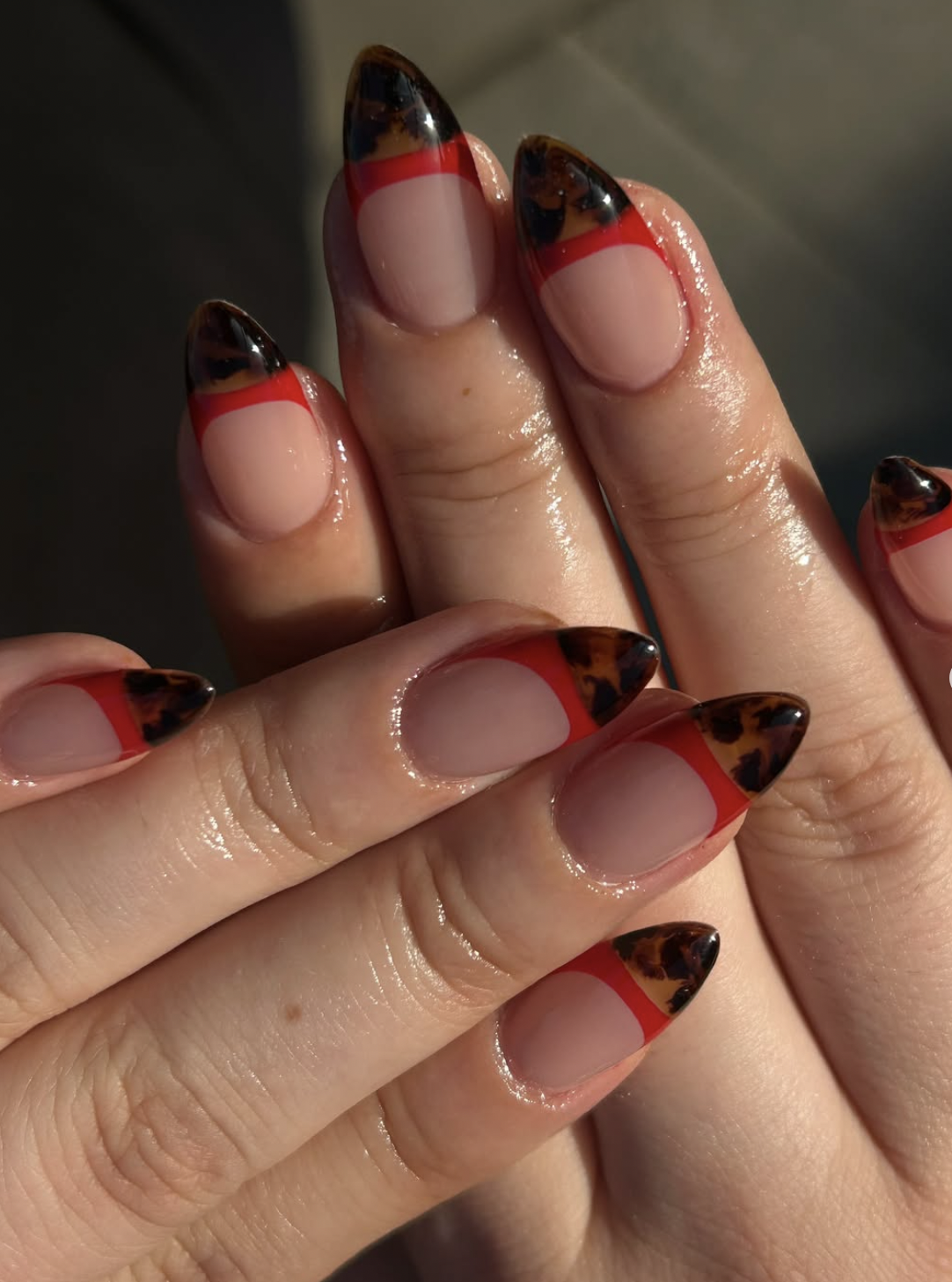 Sheer almond nails with strawberry-red French tips and thin chocolate-brown lines beneath them.