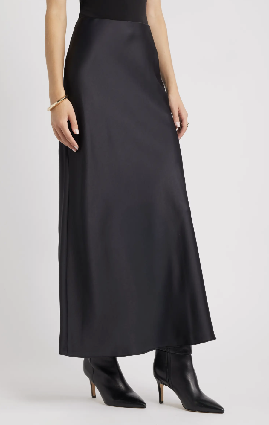 A black satin maxi skirt with a slight sheen, styled with black leather pointed-toe heeled boots, ideal for pairing with flats for women for a more casual look.