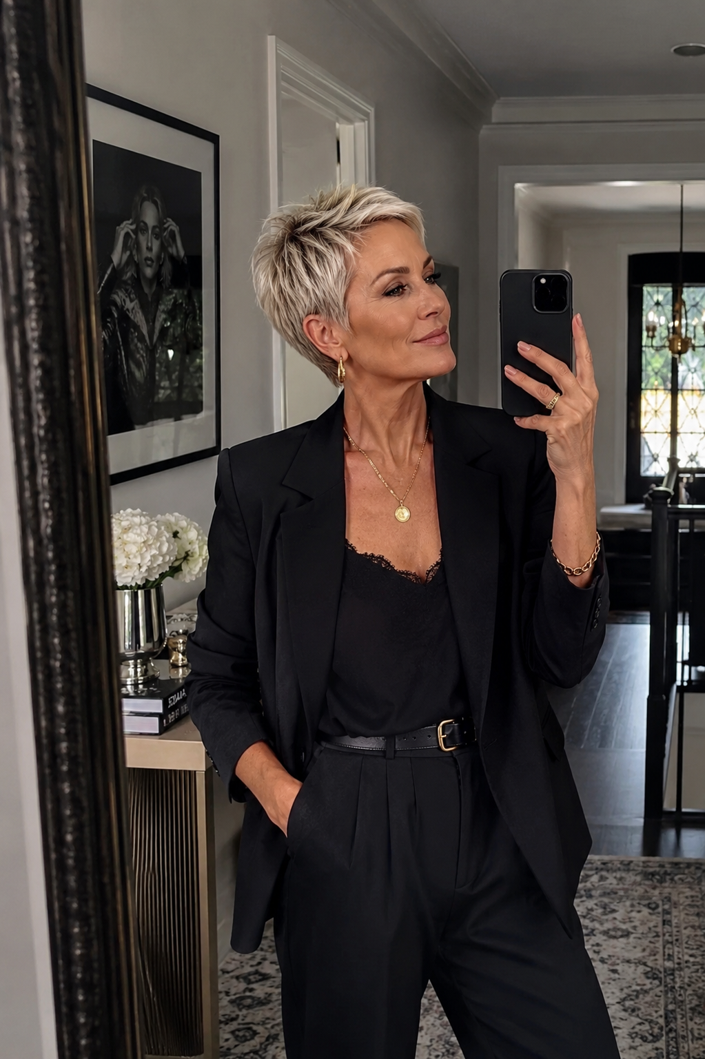 A woman over 50 with a textured, modern silver pixie cut wearing a black blazer and gold necklace.
