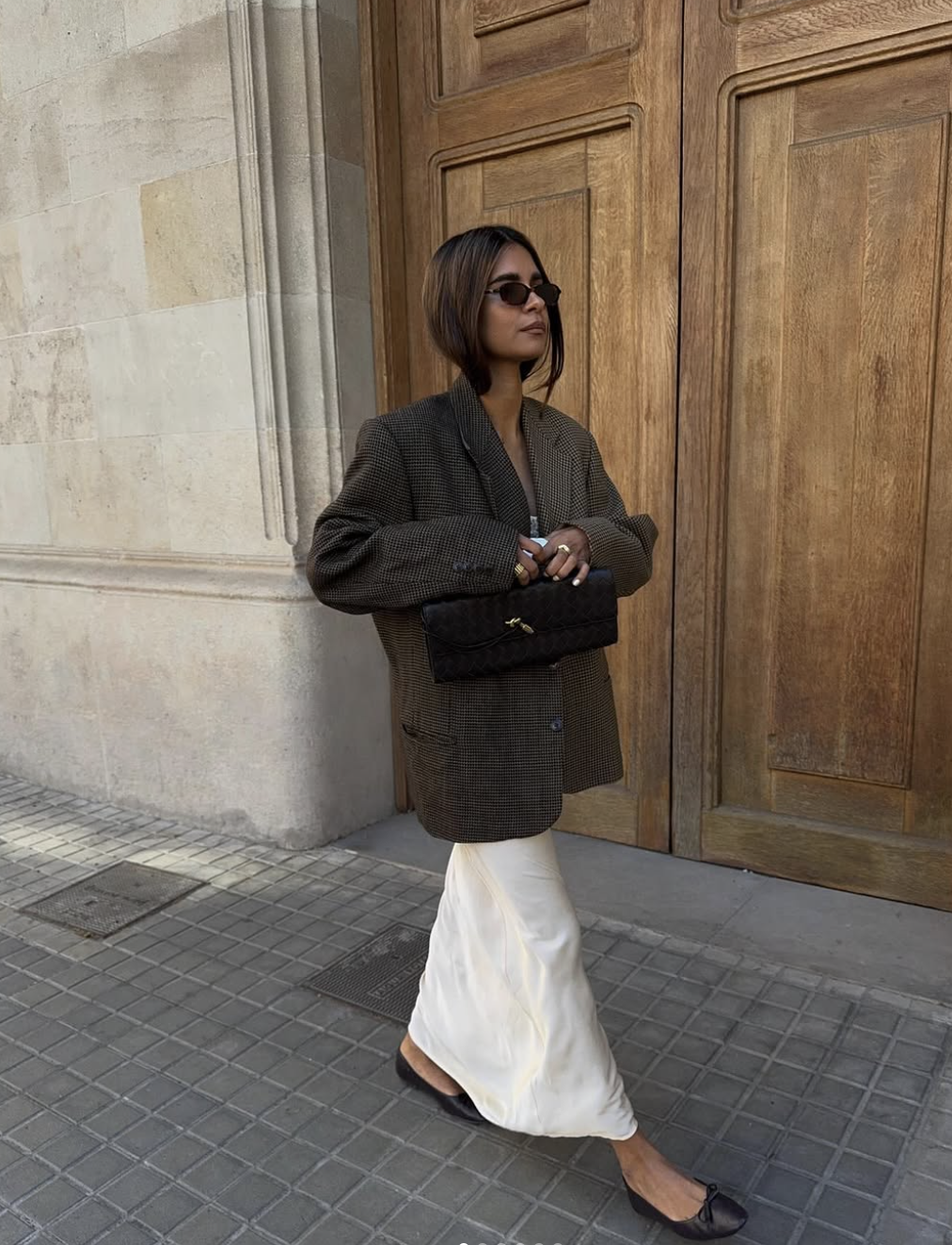 A woman wearing a dark structured blazer layered over a white midi slip dress, demonstrating a balanced "Hard vs. Soft" outfit formula.