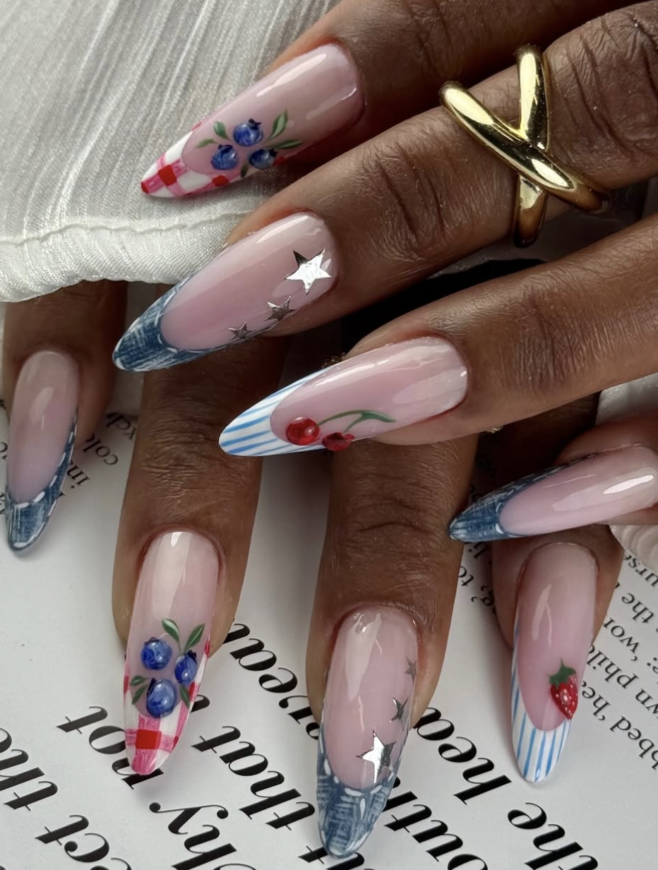 Long, almond-shaped nails featuring a creative 4th of July design with blue denim textures, classic red-and-white gingham plaid, crisp stripes, hand-painted cherries, and reflective silver stars on sheer French tips.