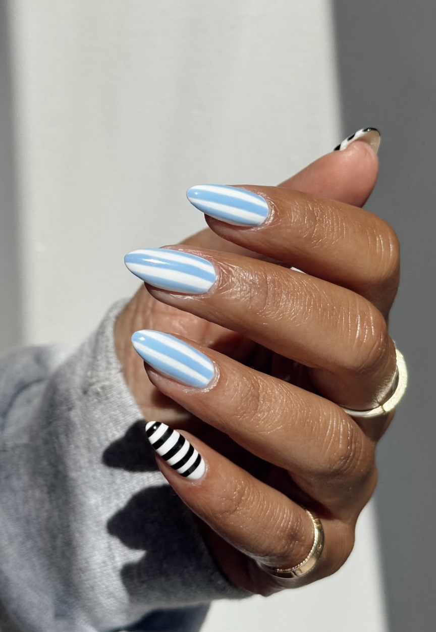 Long oval nails featuring a mix of light blue and white vertical stripes, paired with a black and white striped accent nail, highlighting cute June nail ideas.