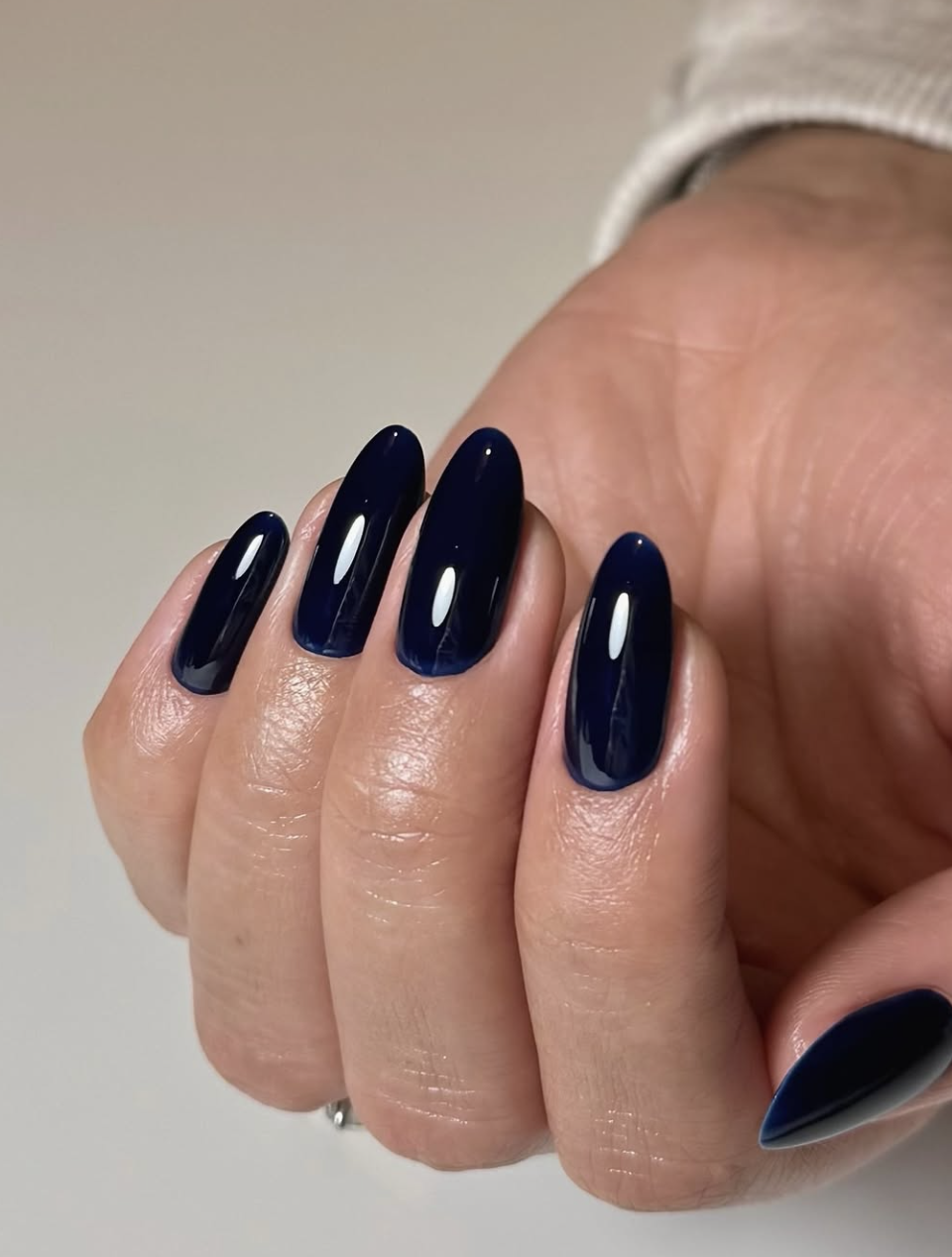 A glossy navy blue Italian manicure on short oval nails, featuring deep blue polish painted with narrow unpainted sidewalls to create an elongated look.