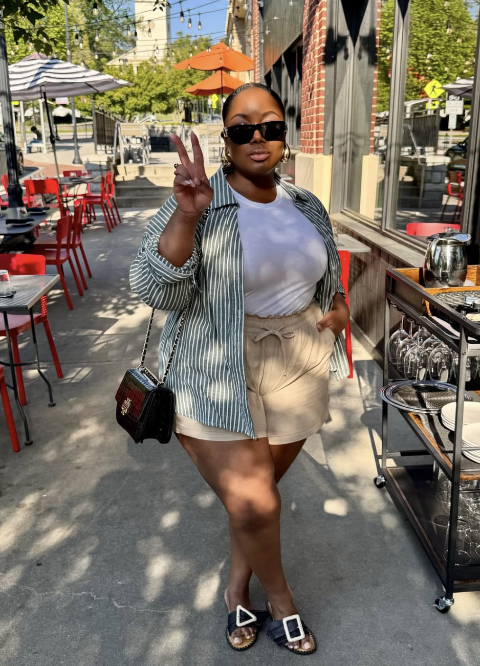 Plus-size woman wearing an unbuttoned green and white striped long-sleeve shirt over a white top, paired with high-waisted khaki shorts featuring a drawstring waist.