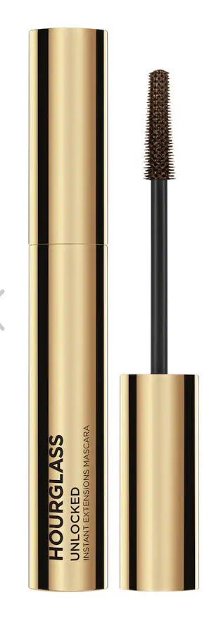 A gold tube of Hourglass Unlocked Instant Extensions Mascara with the thin, molded mascara wand displayed next to the tube