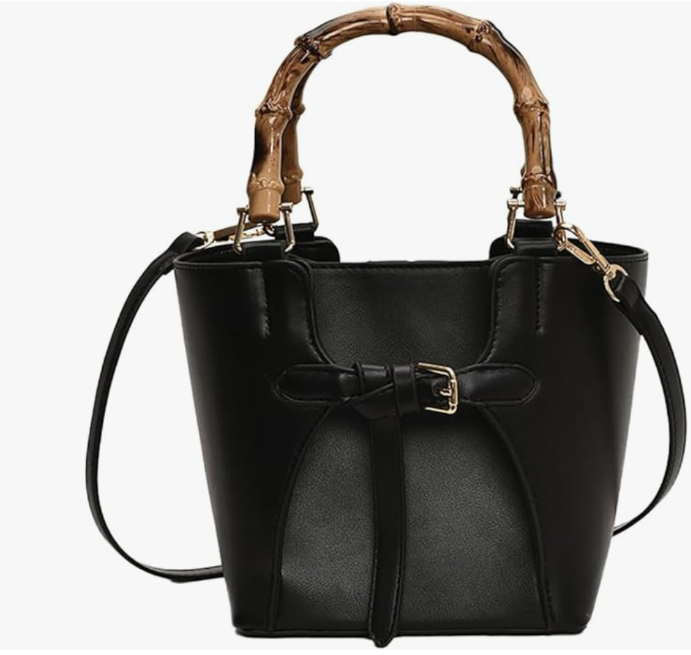 A structured black vegan leather bucket bag featuring a natural bamboo top handle and a removable crossbody strap.