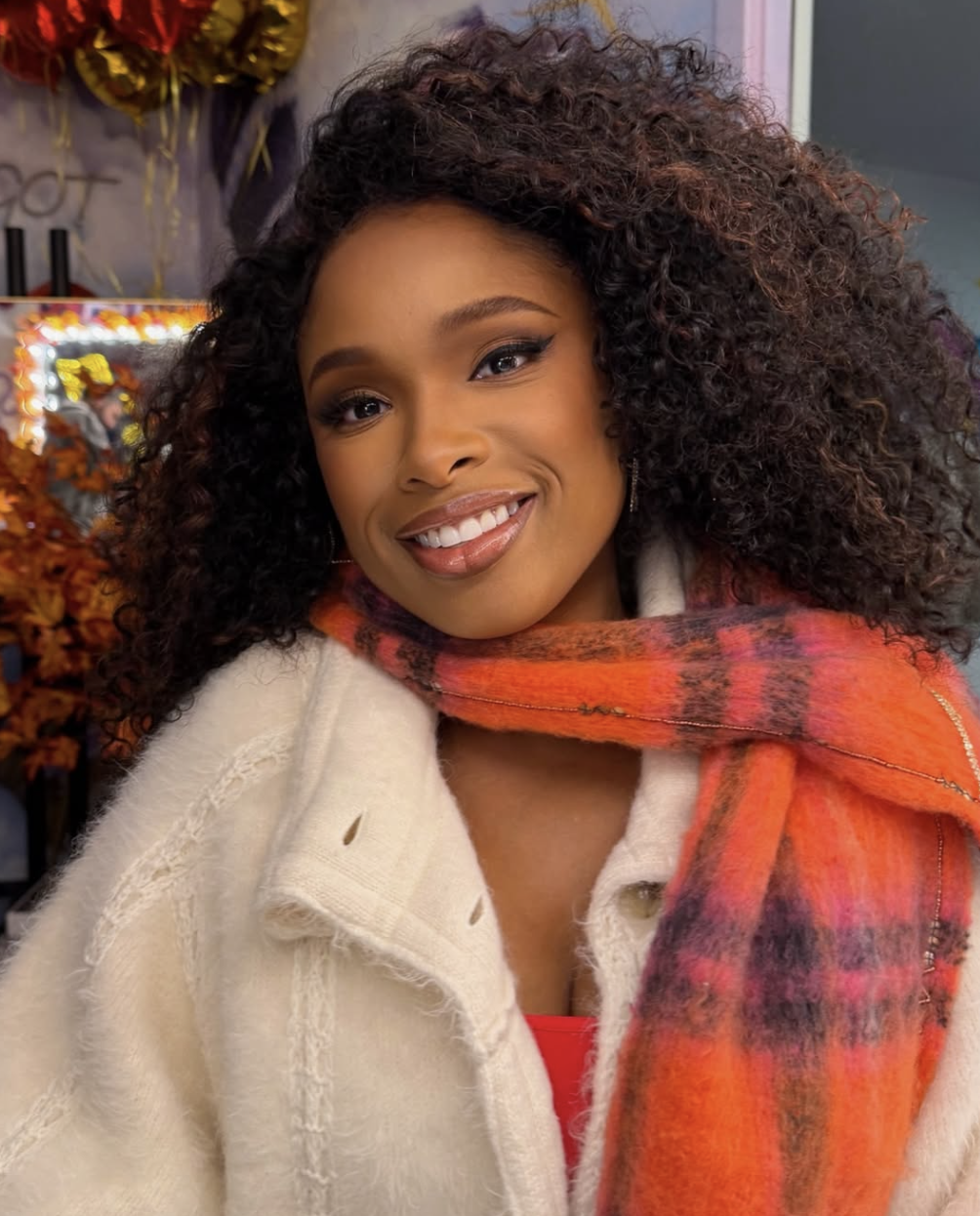 Jennifer Hudson wearing a cream textured coat with a vibrant orange and pink plaid scarf, illustrating how rich, warm tones harmonize with the Deep Autumn season.