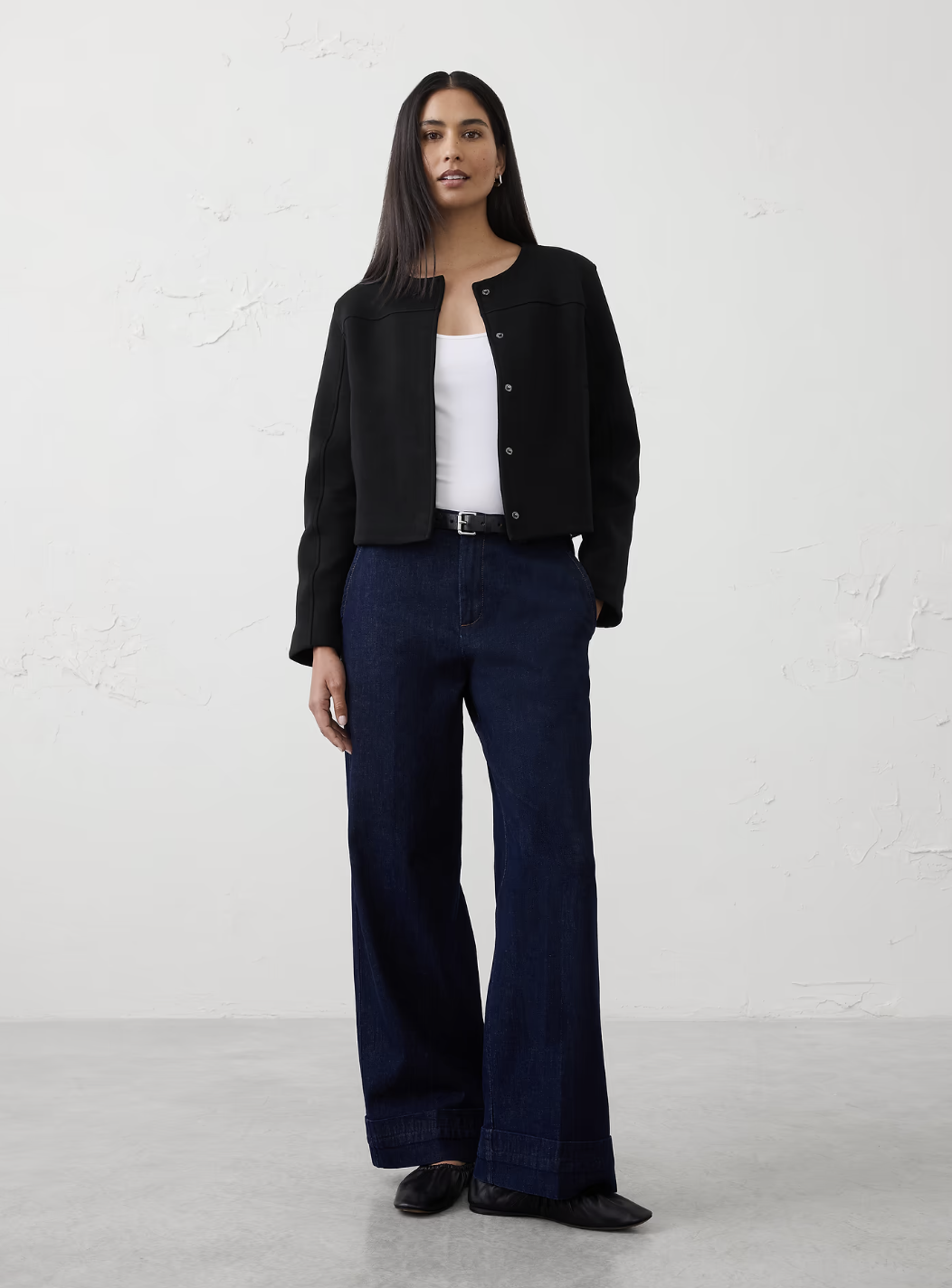 A woman wearing a modern black collarless cropped jacket styled with dark wide-leg trousers for a chic fall workwear outfit.