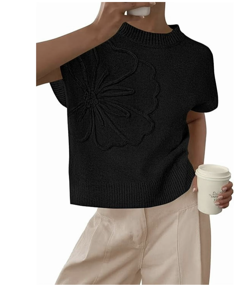 A woman wearing a black short-sleeve crochet sweater with an intricate floral knit pattern, paired with tan linen trousers.