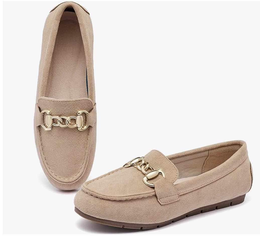 A pair of beige suede loafers with a classic gold horsebit buckle on the top, shown from a side-angle view against a transparent background.