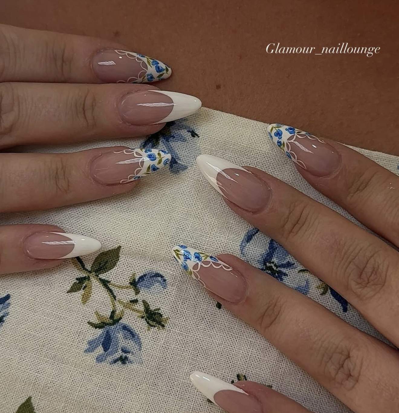 Long almond-shaped French tip nails with delicate blue floral lace patterns bordering the white tips.