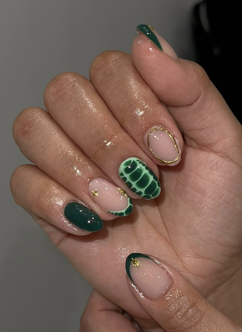 Close-up of short oval nails featuring an olive green micro French tip with delicate gold star accents over a sheer nude pink base.