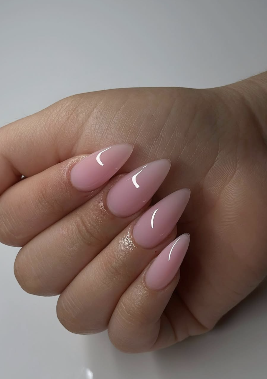 Long almond-shaped nails with a creamy, semi-translucent strawberry milk pink finish and a high-shine reflective top coat.
