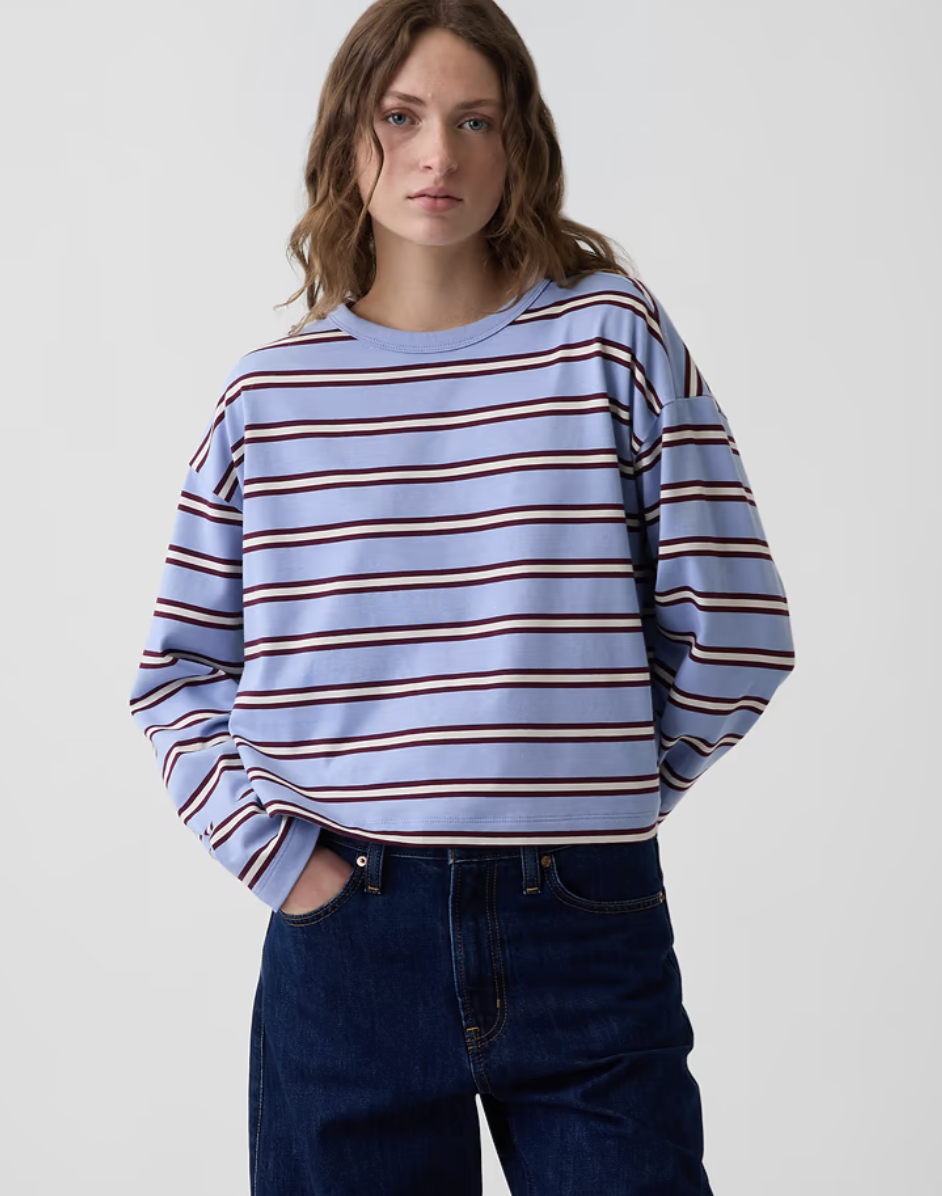 Model wearing a blue and ivory striped boatneck long-sleeve shirt paired with dark-wash jeans.