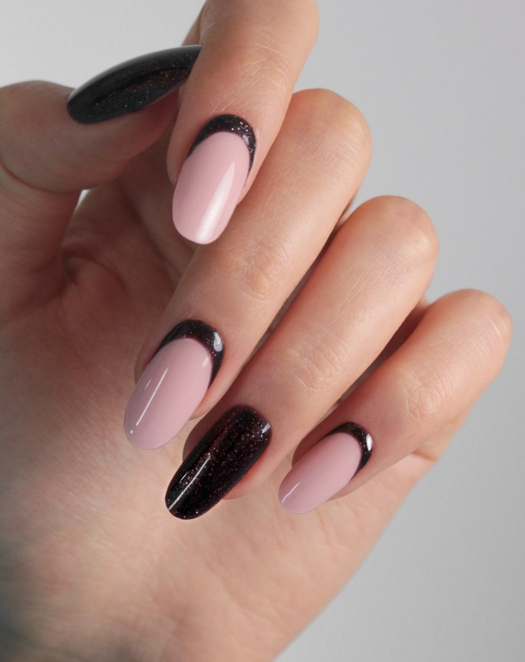 Almond-shaped nails with a soft pink base and a thick, glittery black reverse French tip along the cuticle line.