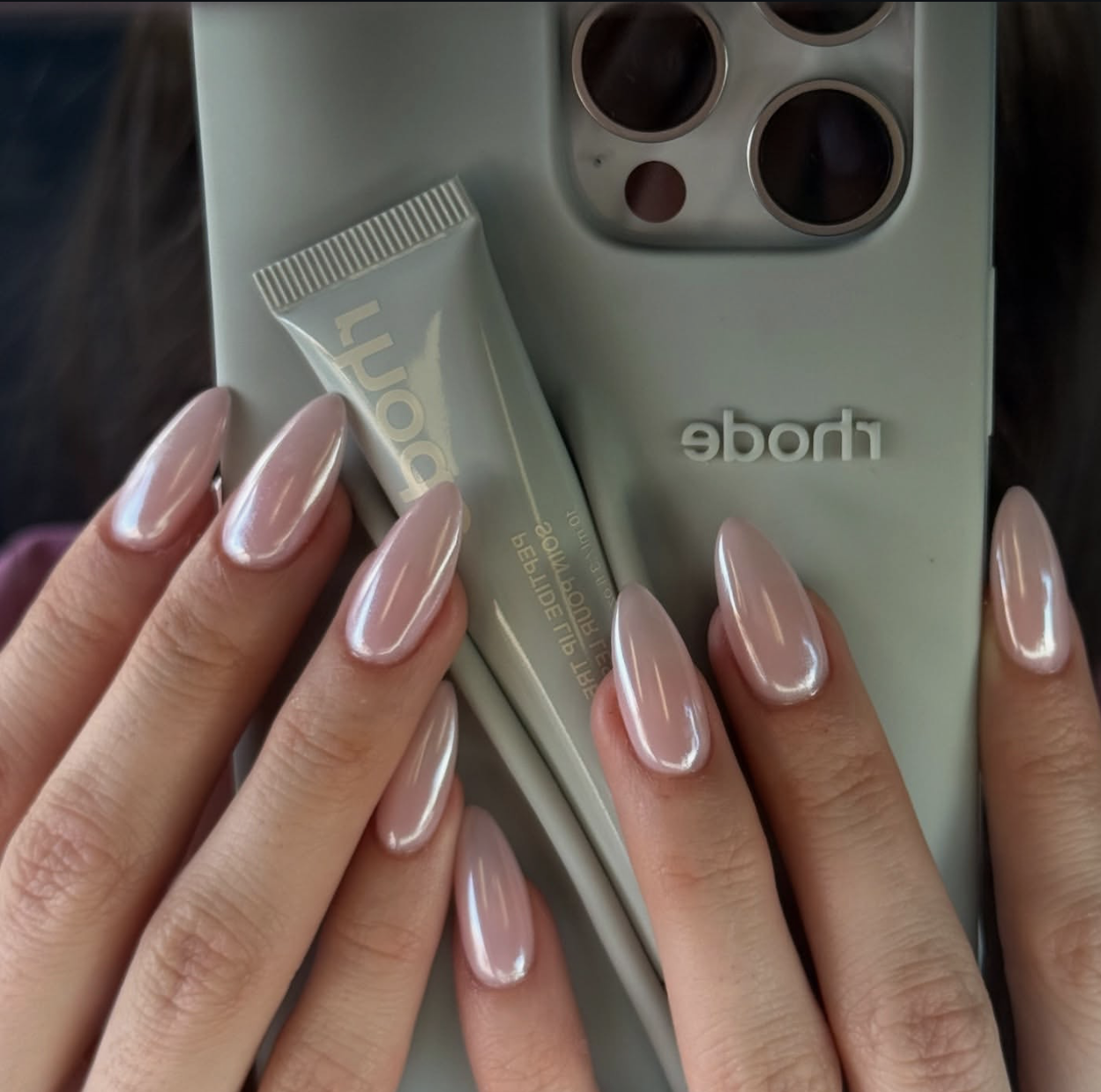 A close-up of short square nails with a milky pink base and a white iridescent chrome "glazed" finish.